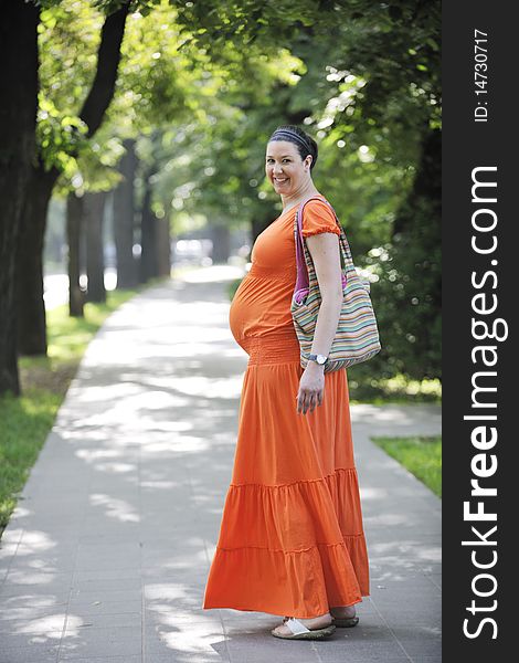 Beautiful young happy pregnant woman outdoor in bright nature in orange dress. Beautiful young happy pregnant woman outdoor in bright nature in orange dress