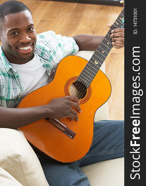 Young Man Relaxing Sitting On Sofa Playing Acoustic Guitar. Young Man Relaxing Sitting On Sofa Playing Acoustic Guitar