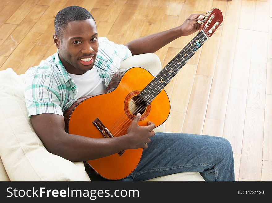 Young Man Relaxing Sitting On Sofa Playing Acoustic Guitar. Young Man Relaxing Sitting On Sofa Playing Acoustic Guitar