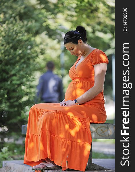 Beautiful young happy pregnant woman outdoor in bright nature in orange dress. Beautiful young happy pregnant woman outdoor in bright nature in orange dress