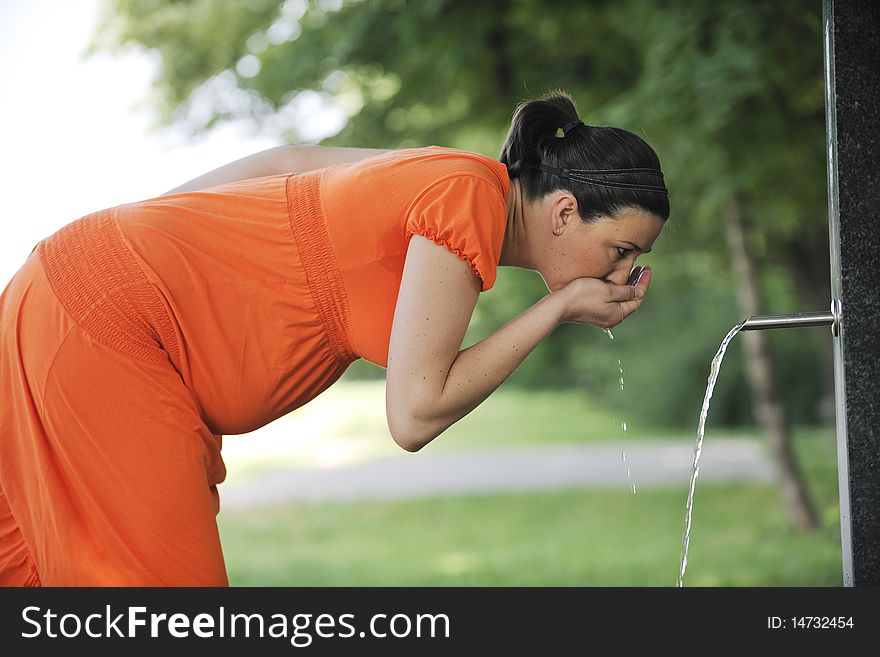 Beautiful young happy pregnant woman outdoor in bright nature in orange dress. Beautiful young happy pregnant woman outdoor in bright nature in orange dress