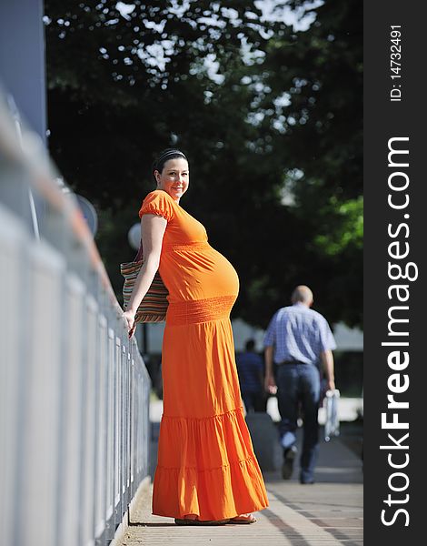 Beautiful young happy pregnant woman outdoor in bright nature in orange dress. Beautiful young happy pregnant woman outdoor in bright nature in orange dress