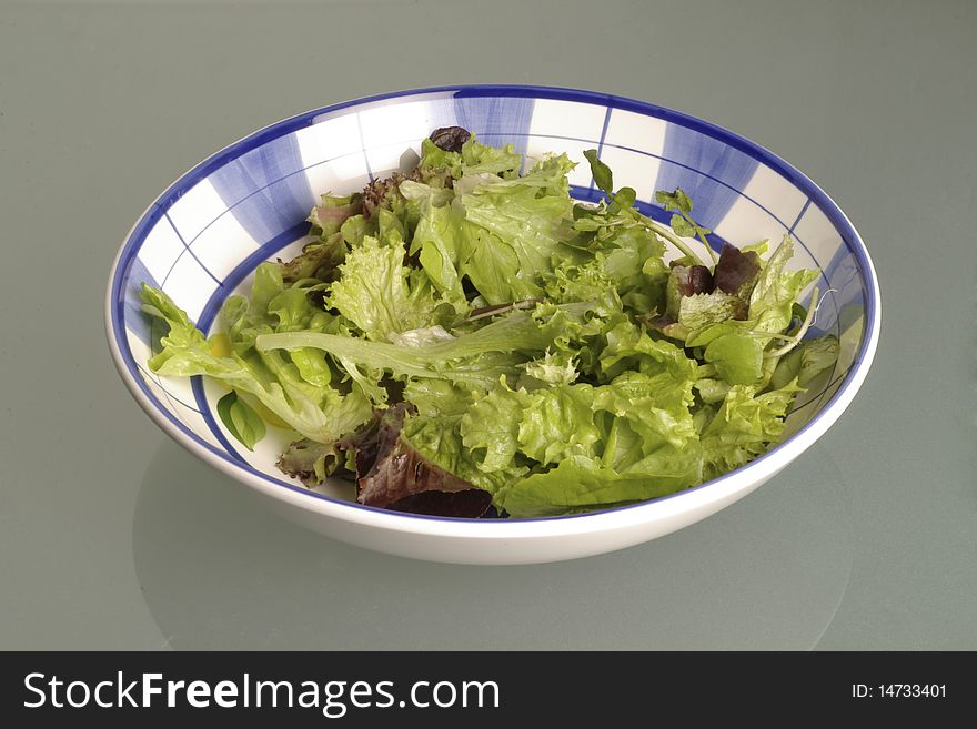 Blue and white bowl filled with salad lettuce leaves on a reflective surface. Blue and white bowl filled with salad lettuce leaves on a reflective surface.