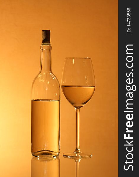 Wineglass near bottle of white wine with reverberation on red-yellow background