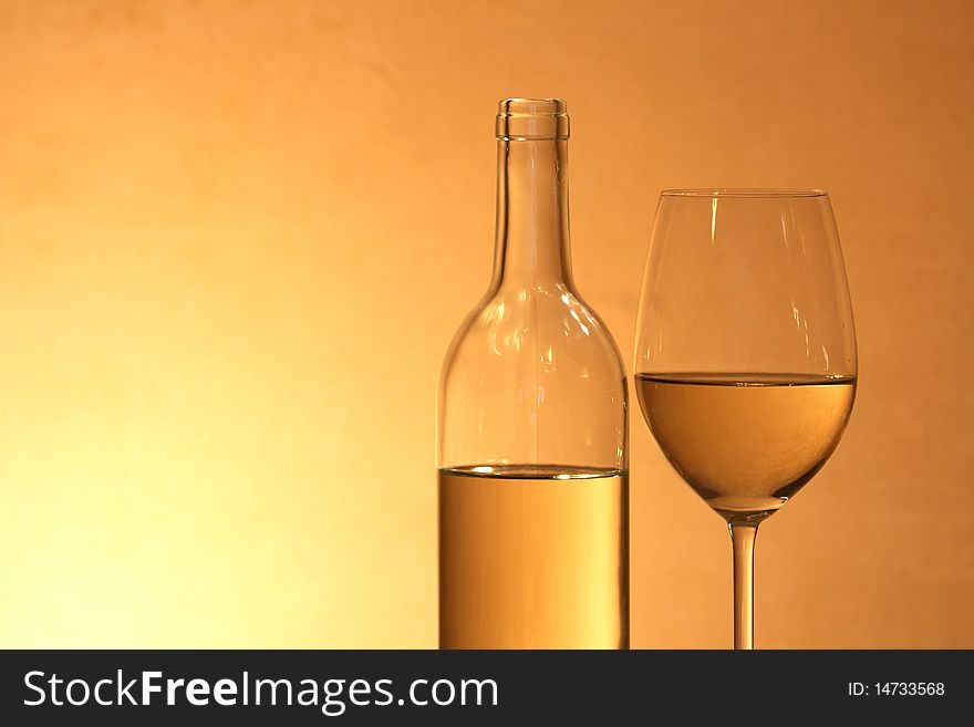Wineglass near bottle of white wine with reverberation on red-yellow background