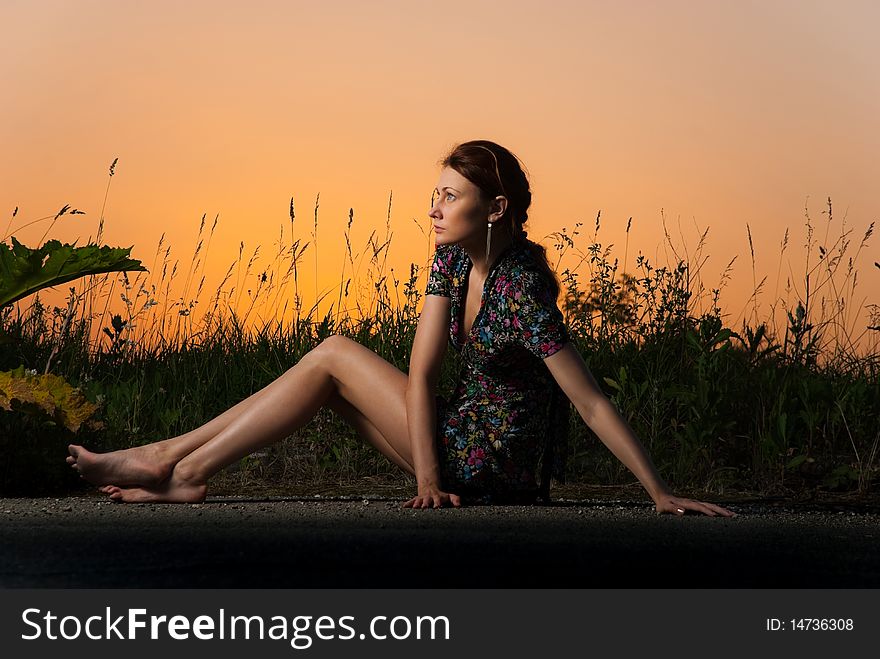 Young redhead woman sitting at summer roadside sunset. Young redhead woman sitting at summer roadside sunset