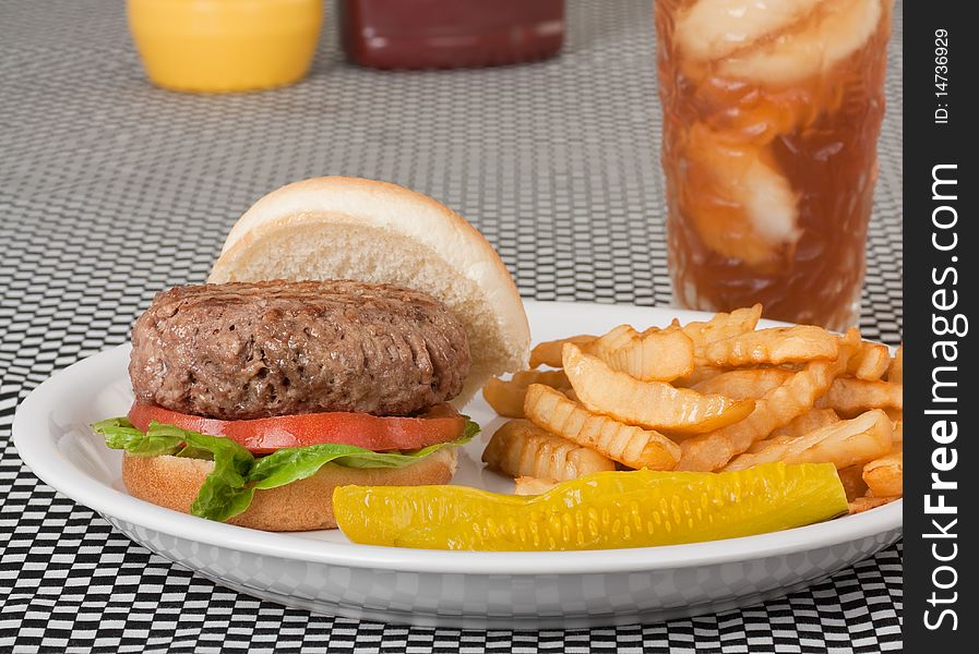 Hamburger on a bun with tomato and lettuce along with french fries, pickle and a drink