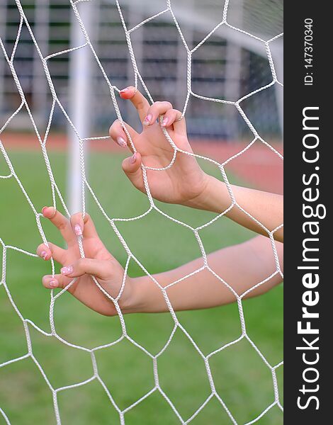 Hand hold on net of soccer goal on sport field.