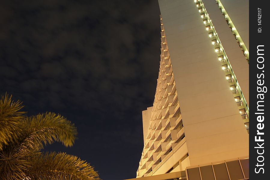 Night scene of a modern apartment in tropical Asia under cloudy sky.