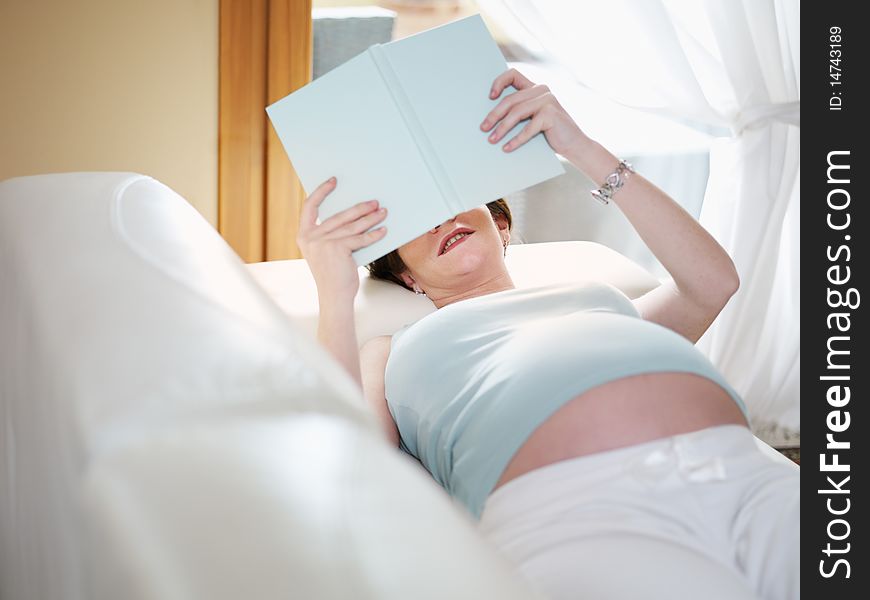 Italian 7 months pregnant woman lying down on sofa and reading book. Horizontal shape, high angle view, Copy space. Italian 7 months pregnant woman lying down on sofa and reading book. Horizontal shape, high angle view, Copy space