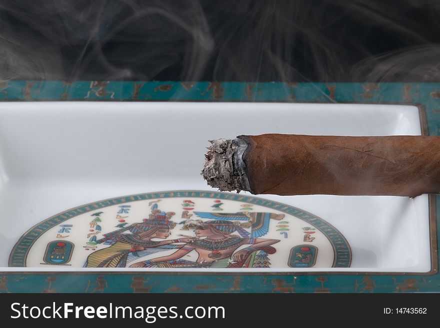 A cigar with curling smoke resting in an ashtray. A cigar with curling smoke resting in an ashtray