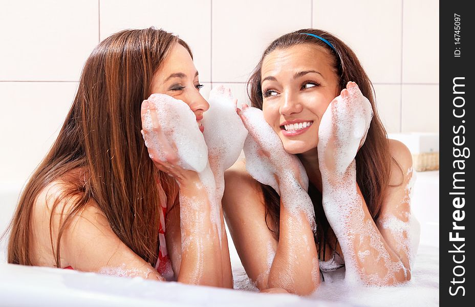 Two tricksy beautiful women in jacuzzi with foam on hands