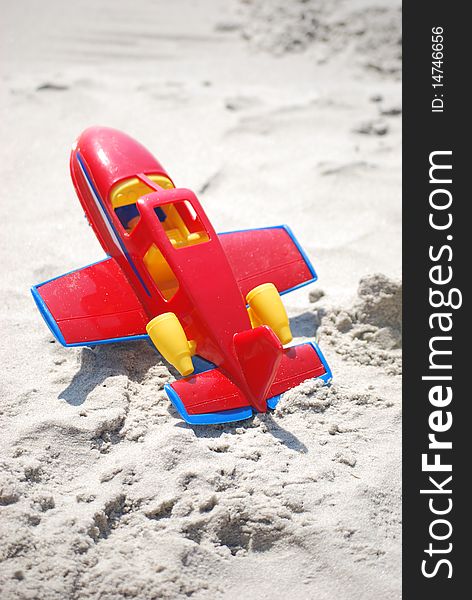 A toy red and yellow airplane laying in the sand on the beach. A toy red and yellow airplane laying in the sand on the beach.