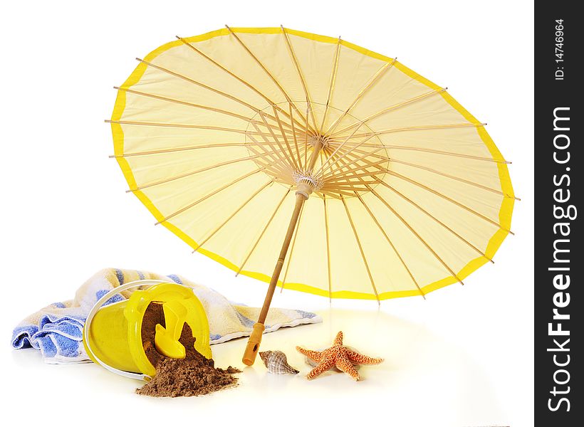 Beach items: a yellow parosal, sand pail with sand and shovel, towel and sea shells. Isolated on white. Beach items: a yellow parosal, sand pail with sand and shovel, towel and sea shells. Isolated on white.