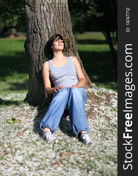 Close-up portrait of young woman taking sun and relaxing sitting under poplar tree. Close-up portrait of young woman taking sun and relaxing sitting under poplar tree
