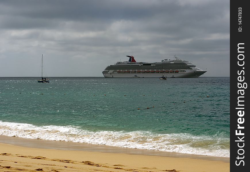 Huge cruise ship anchoring outside the harbor in front of the beach. Sky is cloudy with small patches of sun giving the ocean a beautiful green color. Huge cruise ship anchoring outside the harbor in front of the beach. Sky is cloudy with small patches of sun giving the ocean a beautiful green color