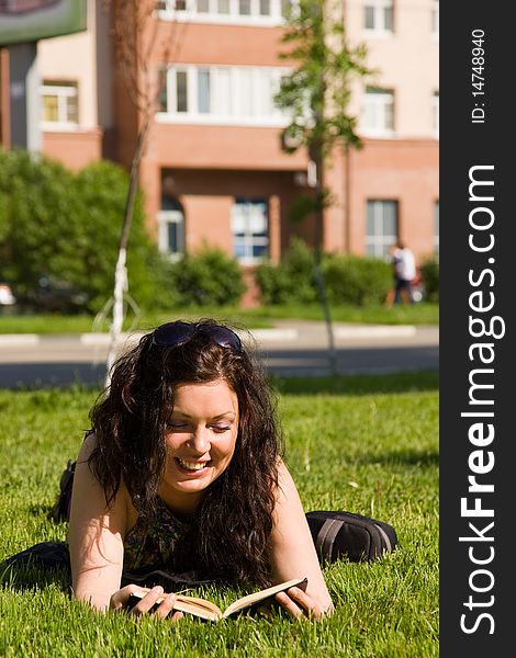 High school student, lying in grass on school campus reading a book. Student studying on the grass. Beautiful young woman reading book at park. High school student, lying in grass on school campus reading a book. Student studying on the grass. Beautiful young woman reading book at park