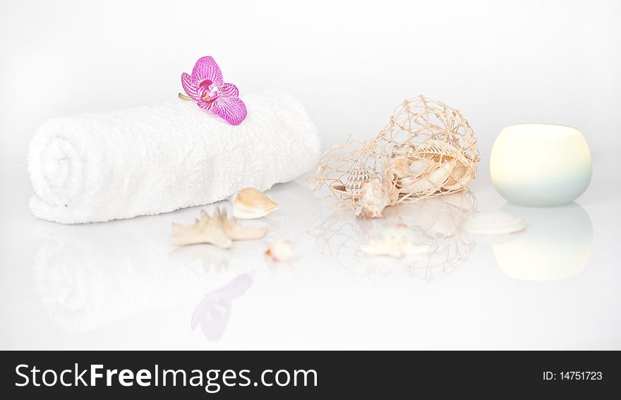 White towel with Orchid, Seashells and a lit candle on white with beautiful reflection. White towel with Orchid, Seashells and a lit candle on white with beautiful reflection.