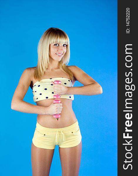 Girl in a yellow holding dumbbells on a blue background. Girl in a yellow holding dumbbells on a blue background