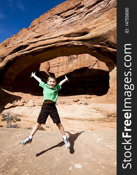 Young boy jumping with outstretched arms and legs while hiking in Arches National Park near Moab UT. Young boy jumping with outstretched arms and legs while hiking in Arches National Park near Moab UT