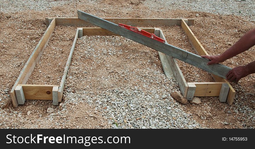 Spirit level and long aluminum ruler checking levels of wooden boards for concrete shuttering.. Builder's hands and arms also in photo. Spirit level and long aluminum ruler checking levels of wooden boards for concrete shuttering.. Builder's hands and arms also in photo