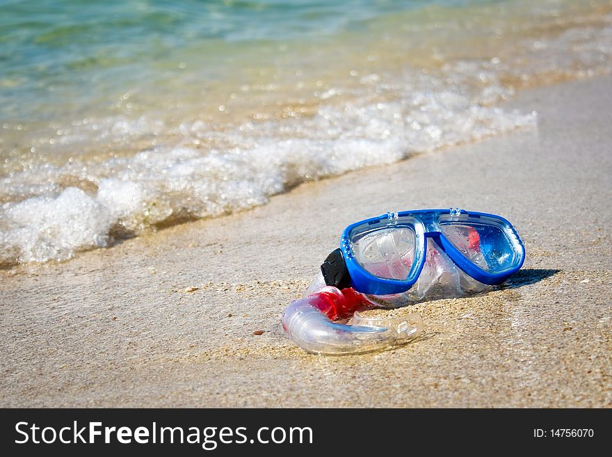 Mask and snorkel lying on sand of beach and washing by surf