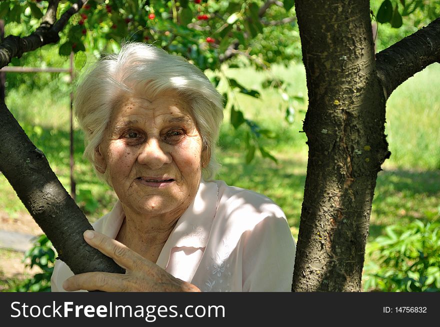 An elderly woman, lost in thought, leaning against a tree. An elderly woman, lost in thought, leaning against a tree