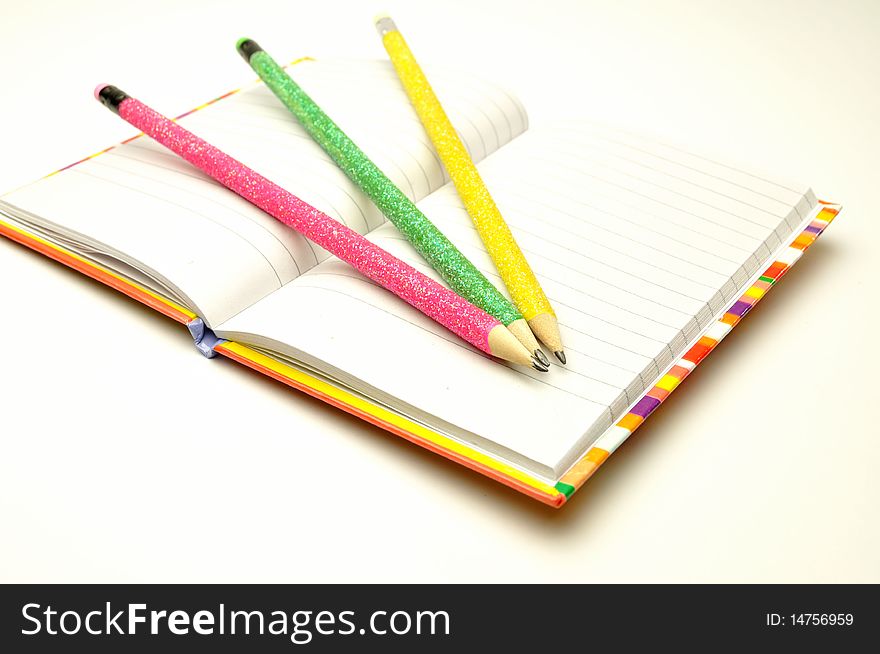 Colored pencils with a notebook on a white background. Colored pencils with a notebook on a white background