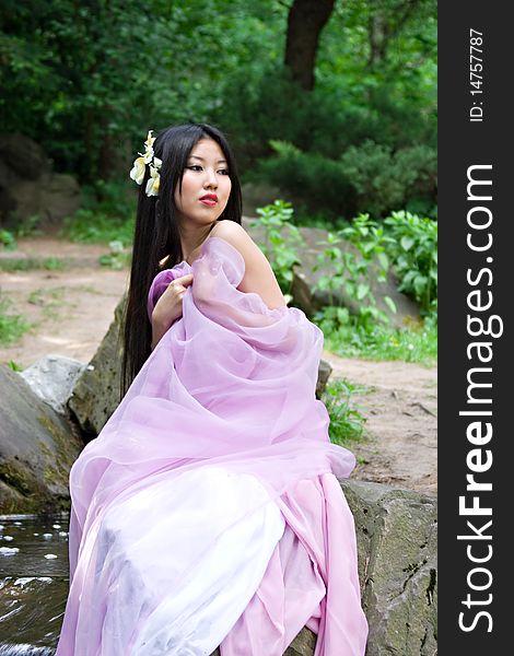 Beautiful Japanese woman in a pink dress sitting on a stone. Beautiful Japanese woman in a pink dress sitting on a stone