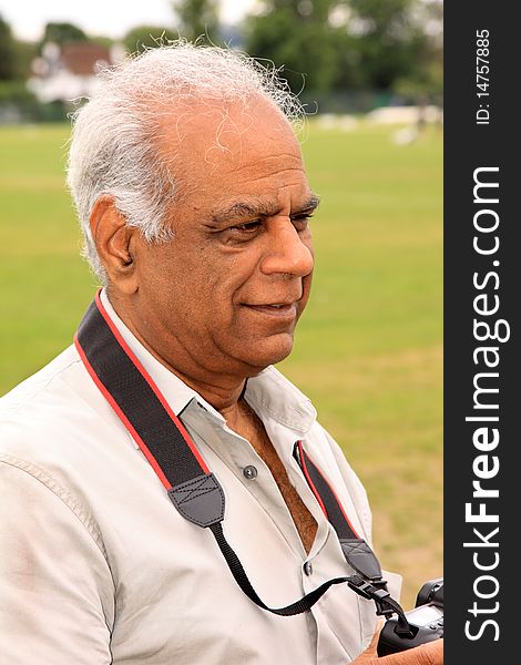 A mature Asian man outdoors in the garden with his camera. A mature Asian man outdoors in the garden with his camera