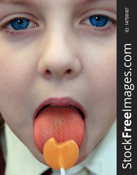 Young blue eyed girl licking an orange lollipop into a heart shape