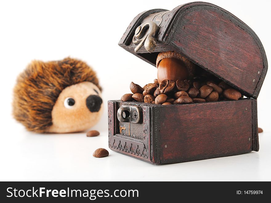 Coffe beans in a chest with an oversized oak nut on top and an hedgehog toy staring at the cest. Coffe beans in a chest with an oversized oak nut on top and an hedgehog toy staring at the cest