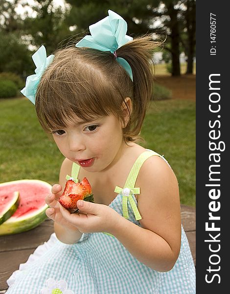Little girl enjoying eating a huge red strawberry outdoors. Little girl enjoying eating a huge red strawberry outdoors.