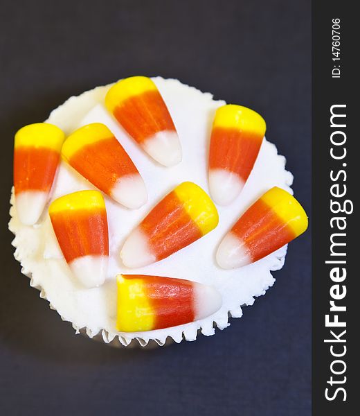 Closeup from overhead of cupcake decorated with vanilla icing and candy corn on a black background. Closeup from overhead of cupcake decorated with vanilla icing and candy corn on a black background.