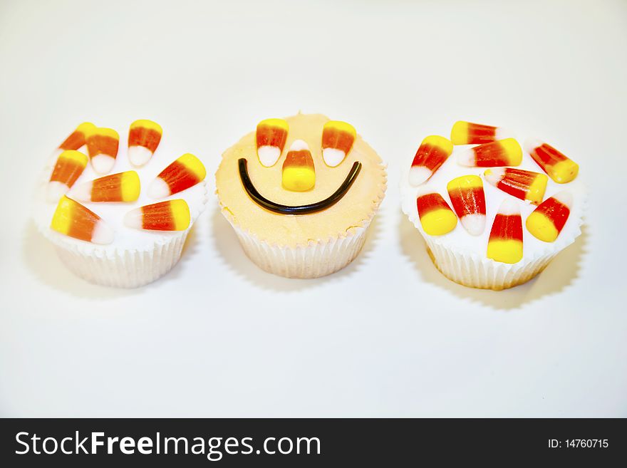 Three halloween cupcakes decorated with frosting and candy corn on a white background