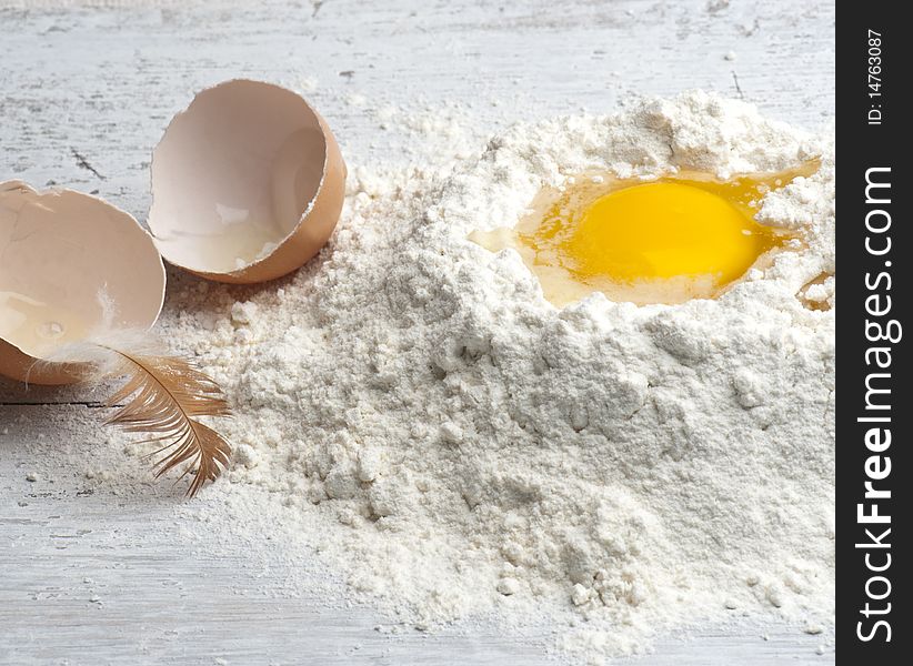 A Cracked Egg In Flour, With Shell and Hen Feather To The Side