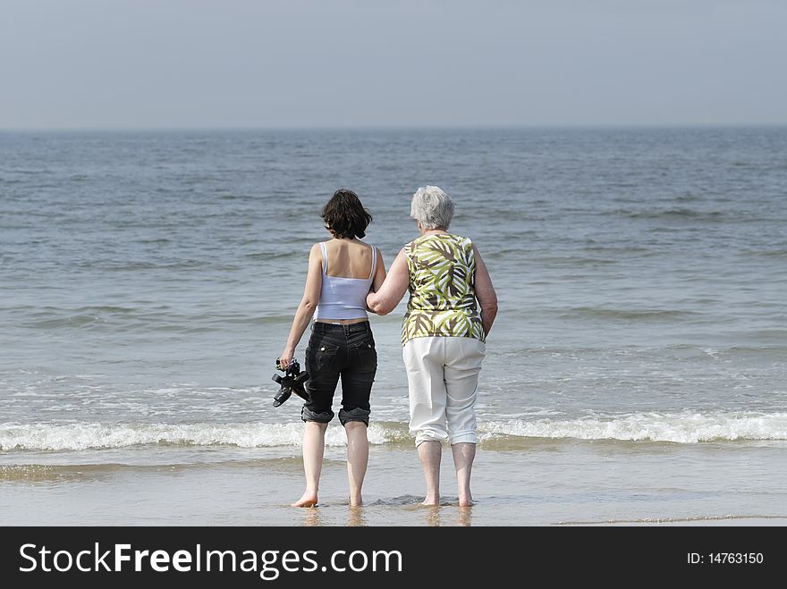 Senior and adult woman looking at the sea with their feet in the water