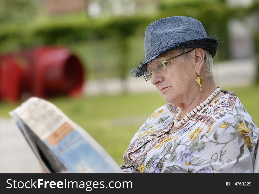 Senior Woman Reading A Newspaper In The Garden