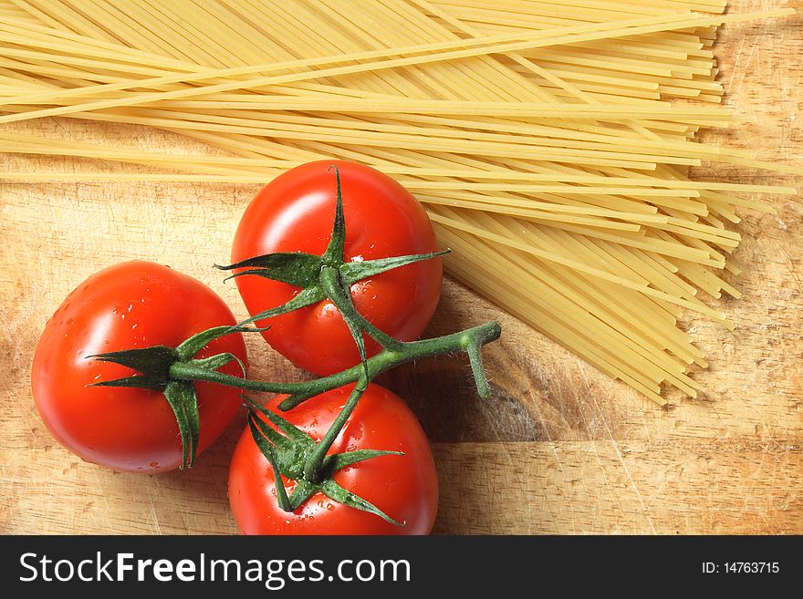 Raw spaghetti and few fresh tomatoes lying on wooden board. Raw spaghetti and few fresh tomatoes lying on wooden board