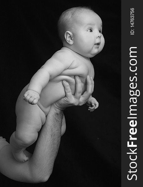 Newborn naked baby in male hands on black background