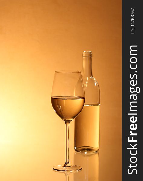 Wineglass near bottle of white wine with reverberation on red-yellow background