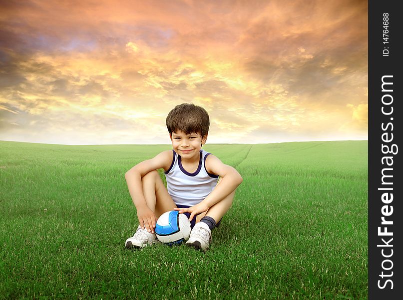 Child sitting on a green meadow with a foot ball in front of him. Child sitting on a green meadow with a foot ball in front of him