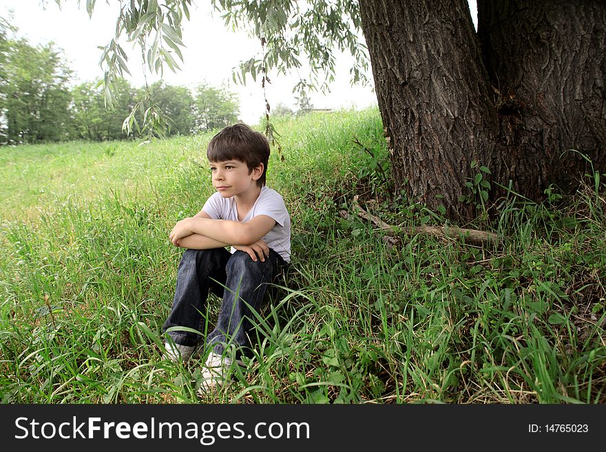 Child sitting under a tree on a green meadow. Child sitting under a tree on a green meadow