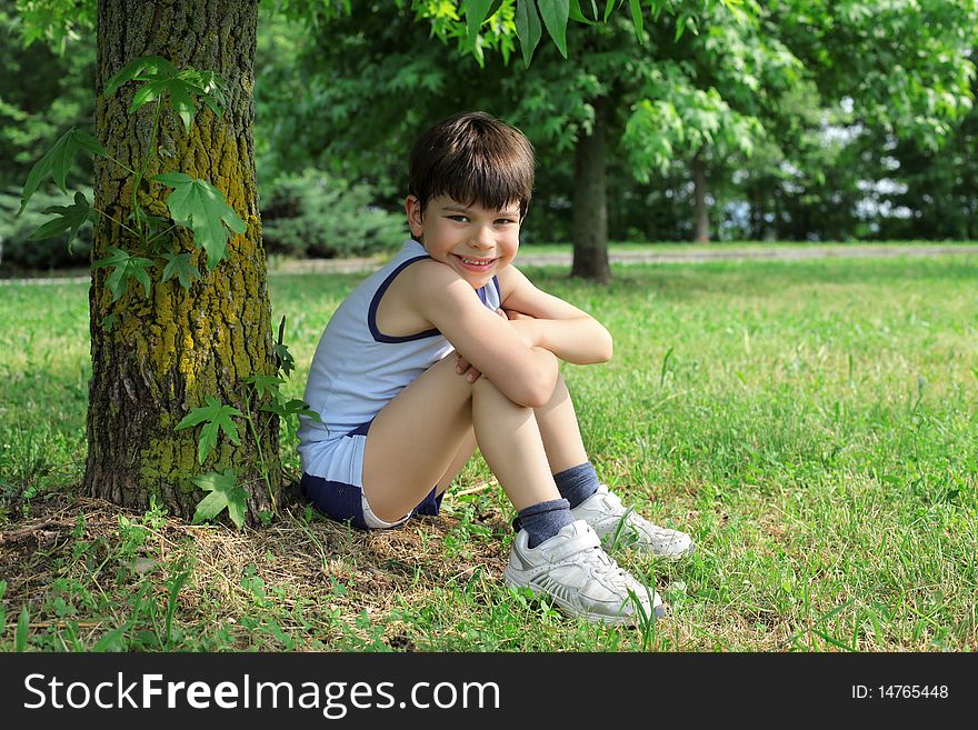 Smiling child sitting under a tree on a green meadow. Smiling child sitting under a tree on a green meadow