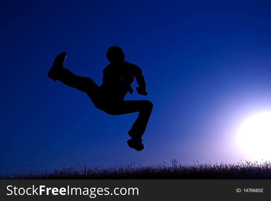 Black silhouette of a jumping young man on a blue sky and sun background. Black silhouette of a jumping young man on a blue sky and sun background