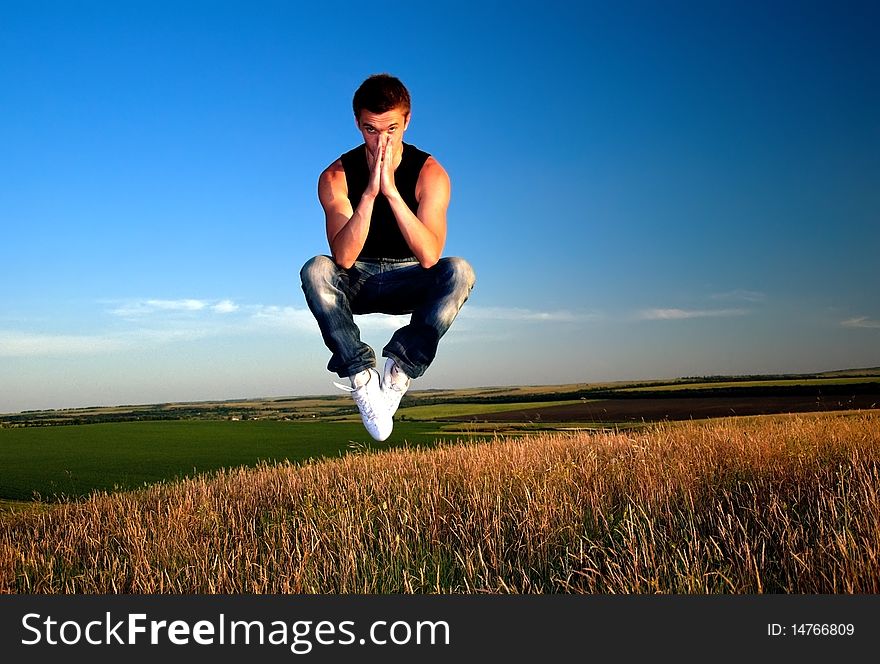 A young man hanging in the air above the meadow against the blue sky. A young man hanging in the air above the meadow against the blue sky