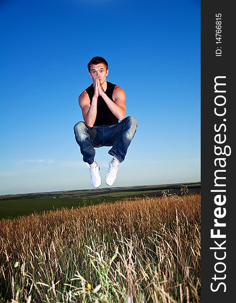 A young man hanging in the air above the meadow against the blue sky. A young man hanging in the air above the meadow against the blue sky