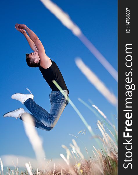 A young man jumping above the meadow against the blue sky. A young man jumping above the meadow against the blue sky