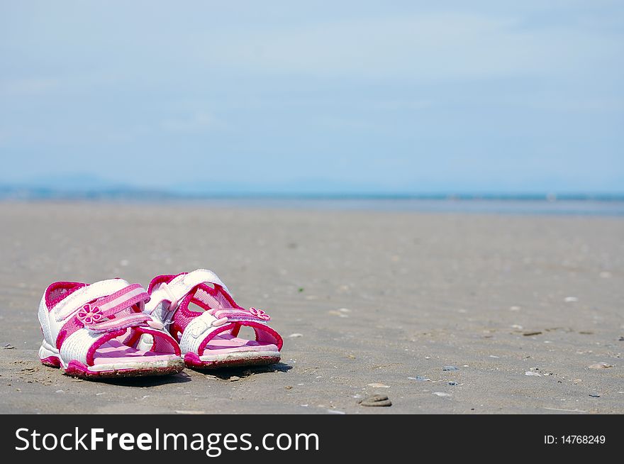 A young girl's sandals on the beach in the sand.