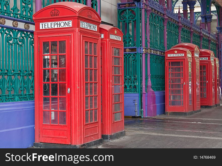 A row of six British telephone boxes set against elaborate wrought iron railings